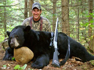 man sitting next to a bear, with his hunting rifle propped up against the bear