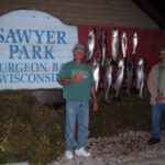 A man standing next to a dozen fish pinned to a Sawyer Park sign