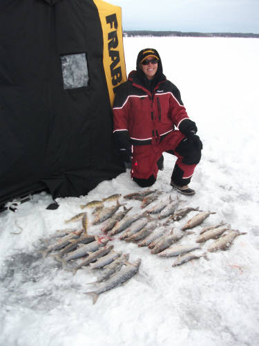 a man kneeling down on the ice next to two dozen fish laid out on the ice in front of a green bay packers branded ice shanty